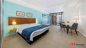 Une chambre d’hôtel comprenant un lit, une table de chevet, une lampe et un coin repas avec des chaises et une table.