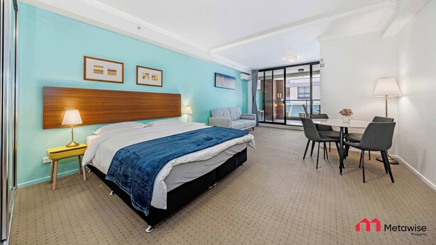 A hotel room with a bed, bedside table, lamp, and a dining area with chairs and a table.
