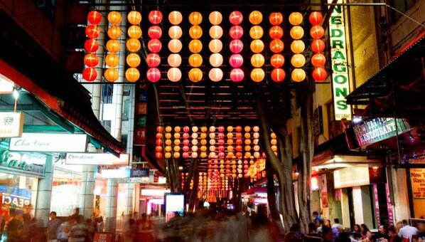 Une rue animée, bordée de lanternes suspendues, de boutiques et d’enseignes indiquant la présence d’un restaurant et d’un hôtel.