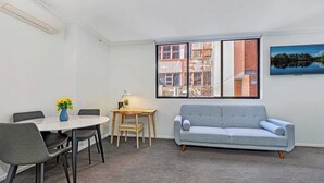 A room with a dining table, chairs, a sofa, a window with a view of buildings, and a painting on the wall. - MetaWise 1Bed Next to ICC Darling Harbour  58 (Sydney)