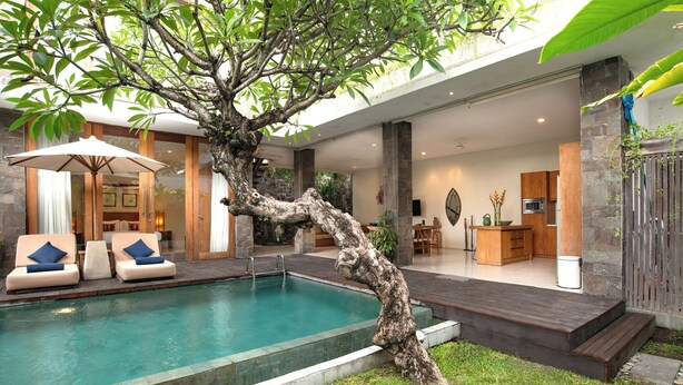 Zona de piscina moderna amb un arbre, seients relaxants i zona de menjador.