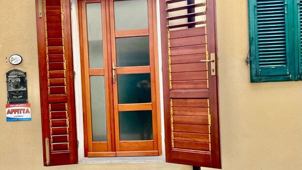 A wooden door with a glass panel, flanked by wooden shutters, and a small step leading to a stone entrance. - Casa Cavour a Capoliveri - Elba Affitti (Capoliveri)