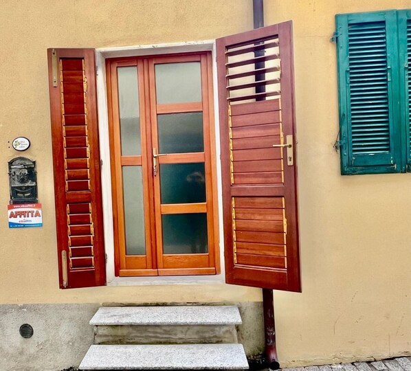 A wooden door with a glass panel, flanked by wooden shutters, and a small step leading to a stone entrance.