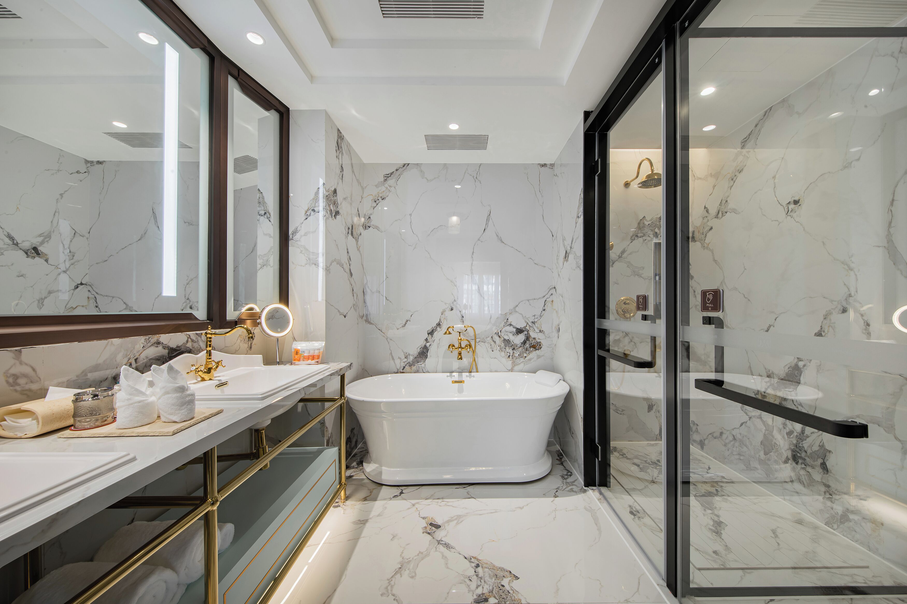 Un baño moderno con una bañera independiente, paredes de mármol y un mueble de tocador con detalles dorados.