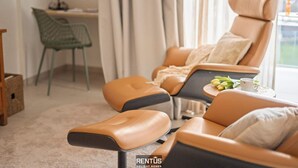 Ein modernes Wohnzimmer mit einer Couch und einem Sessel, einem kleinen Tisch mit einer Tasse und Zitronen sowie einem Schreibtisch mit einer Lampe.
