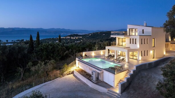 Une maison moderne à deux étages avec piscine, située sur une colline et offrant une vue sur la mer et les montagnes.