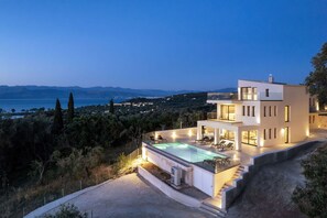 Une maison moderne à deux étages avec piscine, située sur une colline et offrant une vue sur la mer et les montagnes.