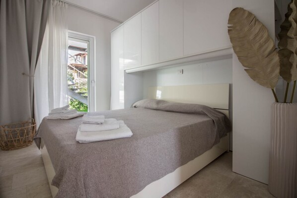 A bedroom with a bed, a window, a white wardrobe, and a large leaf decoration.