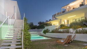 Une maison moderne dotée d’une piscine, d’un espace salon extérieur et d’un escalier menant à un étage supérieur.