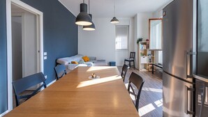 A modern kitchen with a wooden dining table, black pendant lights, and a stainless steel refrigerator.