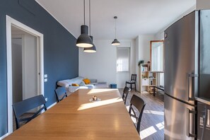 Una cocina moderna con una mesa de comedor de madera, lámparas colgantes negras y un refrigerador de acero inoxidable.