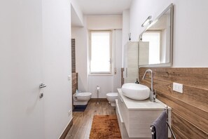 Un baño moderno con tocador de madera, un espejo grande, un bidé y un inodoro.