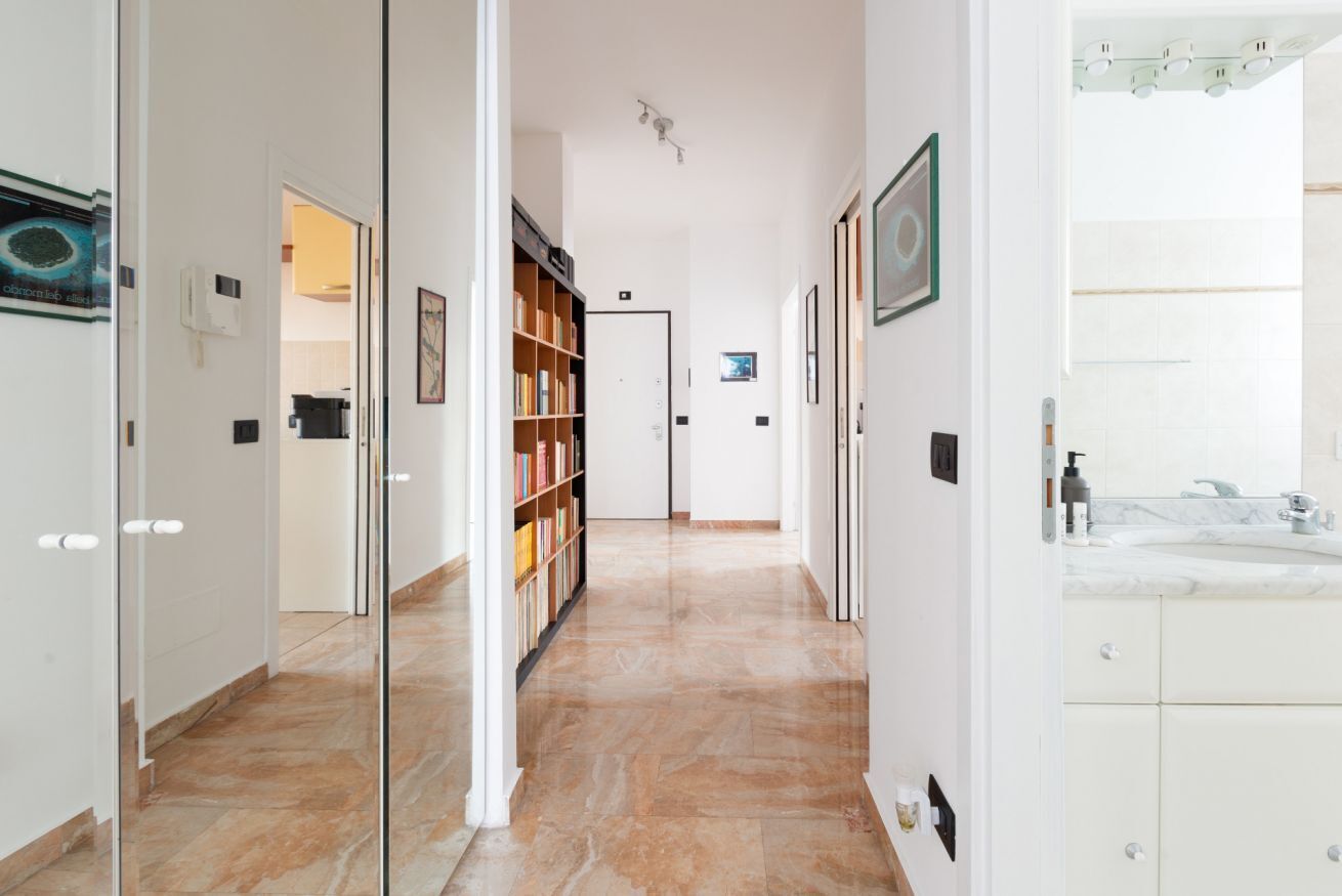 A hallway with a glass partition, a bookshelf, a door, and a bathroom with a marble countertop.