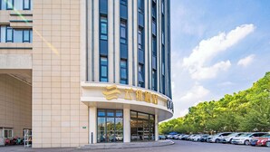 A hotel with a modern facade, large windows, and a parking lot with several cars. - U-FREE Hotel Shanghai Hongqiao Wuzhong (Shanghai)