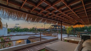 A rooftop terrace with a wooden deck, a cushioned seating area, and a view of the surrounding landscape. - Villa Dusa  (Canggu)
