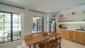 A modern kitchen with wooden cabinets, a large island, and a view of a pool. - Villa Dusa  (Canggu)
