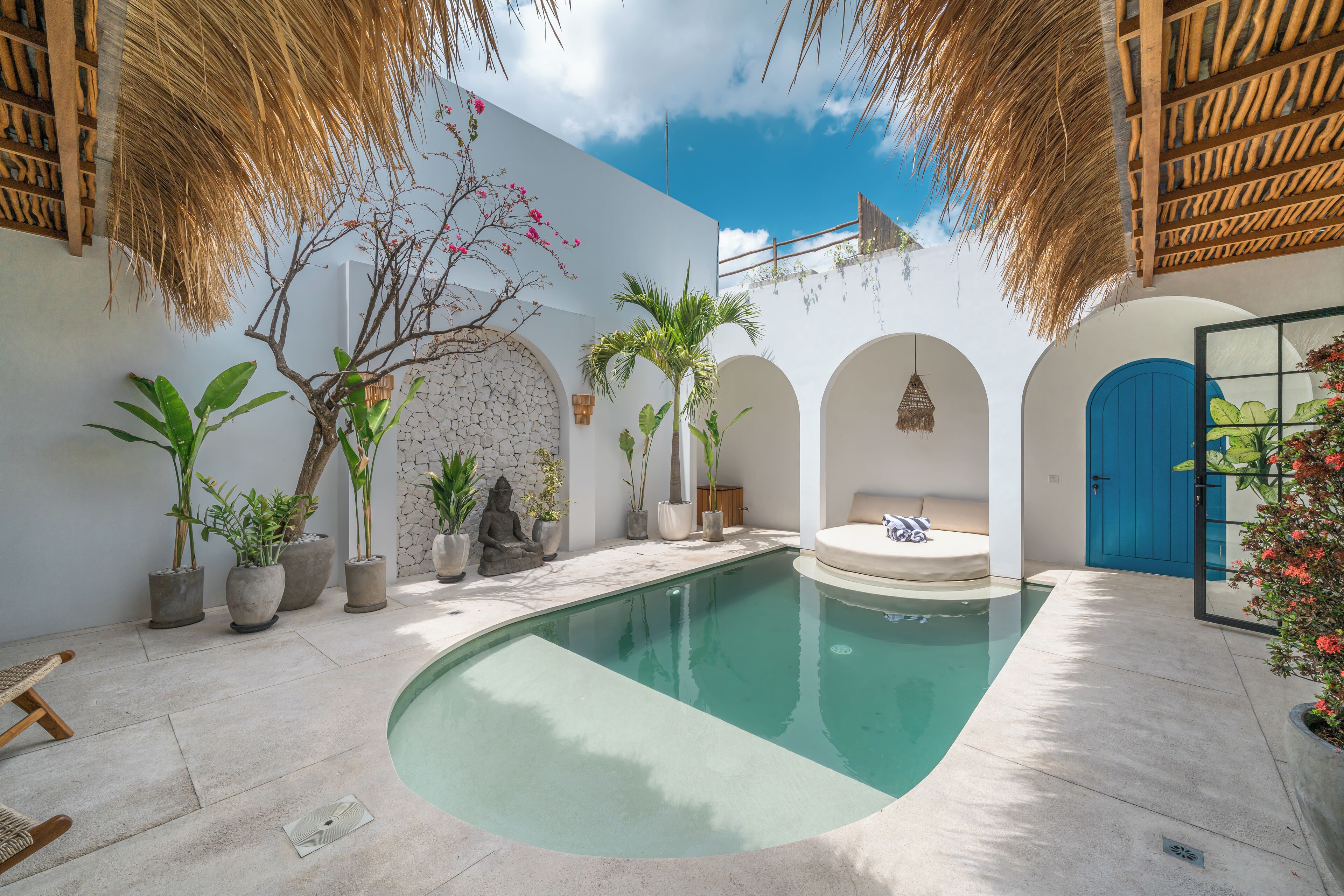 A pool area with a curved pool, potted plants, a blue door, and a stone wall.