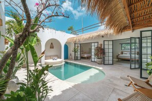 A poolside area with a thatched roof, a lounge chair, and a bed with a view.