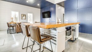 Una cocina moderna con encimera de madera, taburetes de bar, horno integrado y televisor montado en la pared.