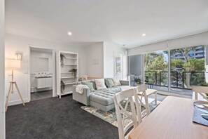 A modern living room with a grey sofa, a dining table, and a balcony with a view of the city.