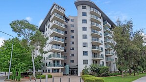 A modern multi-story residential building with balconies, a landscaped entrance, and a clear sky. - Central Braddon Retreat with Balcony & Pool Access (Turner)