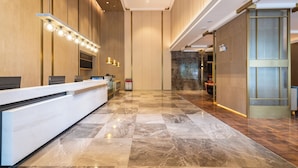 Un hall d’hôtel avec un sol en marbre, un comptoir d’accueil et un luminaire fixé au mur.