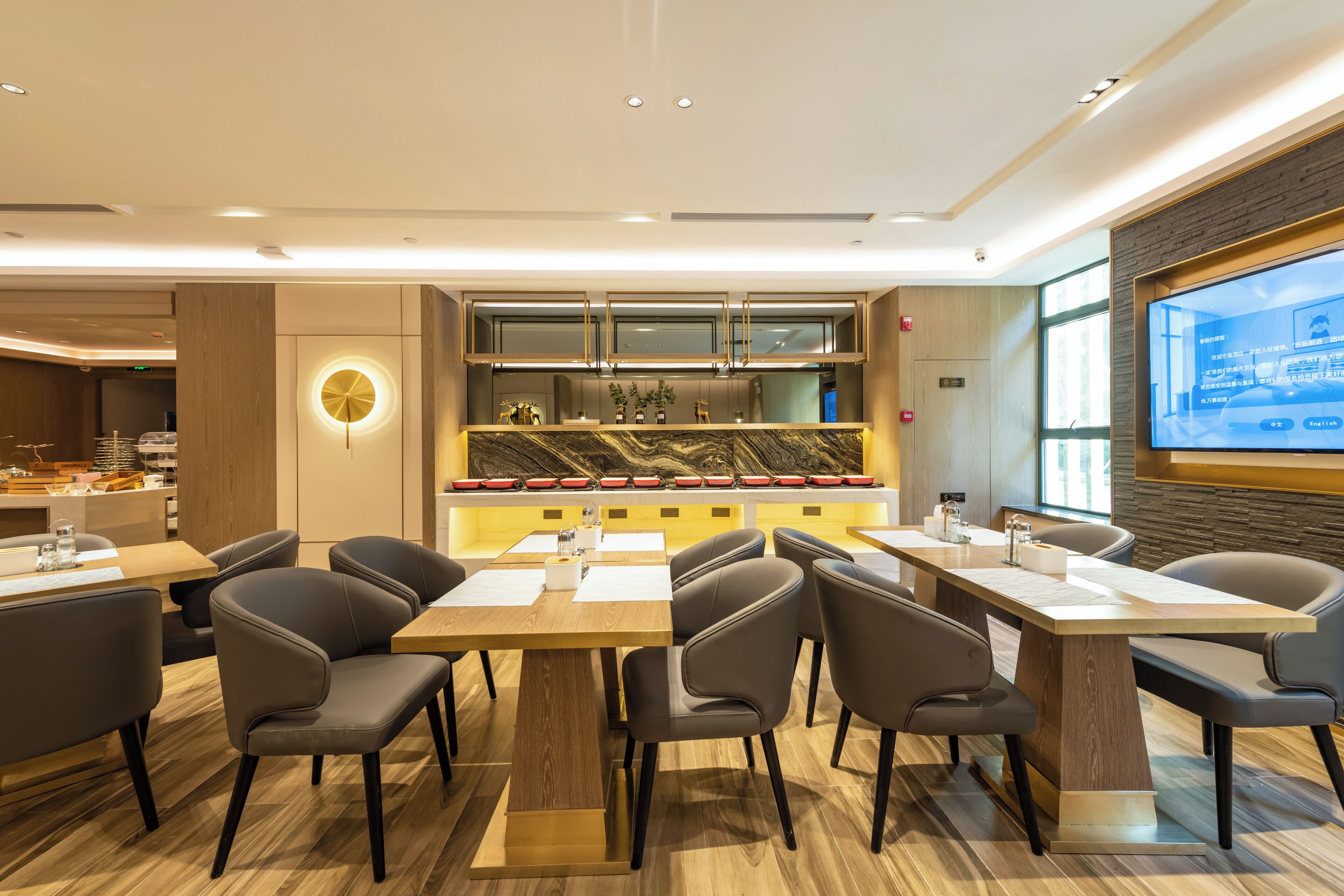 A modern restaurant with a central bar, multiple seating areas, and a large screen displaying content.