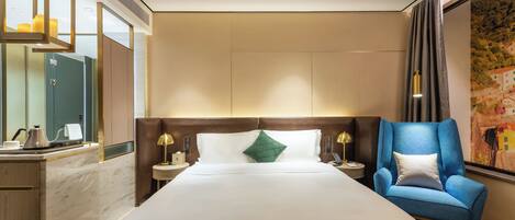 Ein Hotelzimmer mit einem großen Bett, einem blauen Sessel, einem Schreibtisch mit Lampe und einem großen Fenster mit Vorhängen.