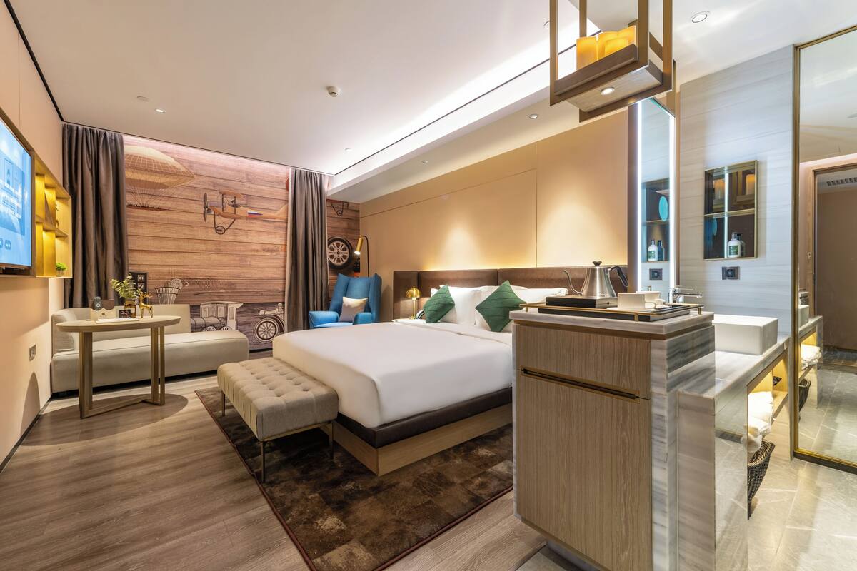 Quarto de hotel moderno com uma cama grande, uma escrivaninha, um sofá e um banheiro com espelho e pia.