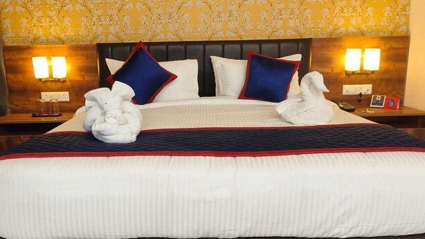 A hotel room with a large bed, two bedside tables, a nightstand, a blue armchair, and floral wallpaper. - Zip By Spree Hotels Dwarka (Dwarka)