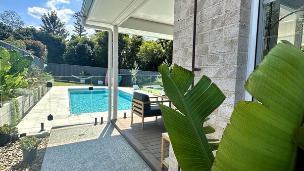 A swimming pool with a wooden deck, a covered seating area, and a stone wall. - The Mermaid's Retreat - Pool in Kiama! (Kiama)