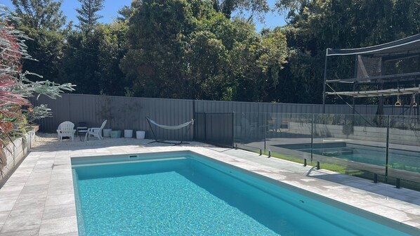A rectangular swimming pool with a tiled deck, surrounded by a fence and trees. - Book 4 nights, Pay for 3 - School Holidays - Message to receive offer! (Kiama)
