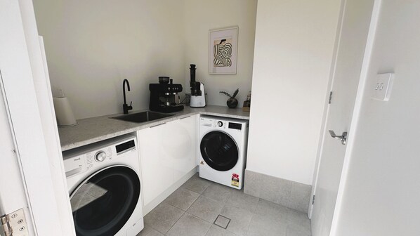 A compact kitchen with a washing machine, a coffee maker, and a sink.