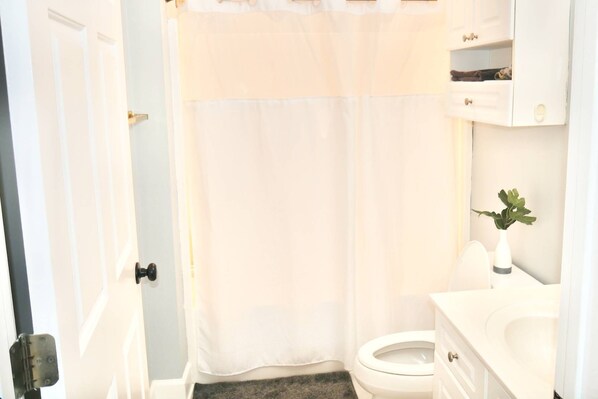 Un baño con inodoro, lavamanos y mueble blanco, además de una cortina de ducha.