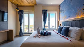 A hotel room with a large bed, a flat-screen TV, and a view of the outdoors through the windows.