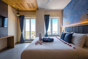 A hotel room with a large bed, a flat-screen TV, and a view of the outdoors through the windows. - HOTEL TAMIZH GRAND (Puducherry)