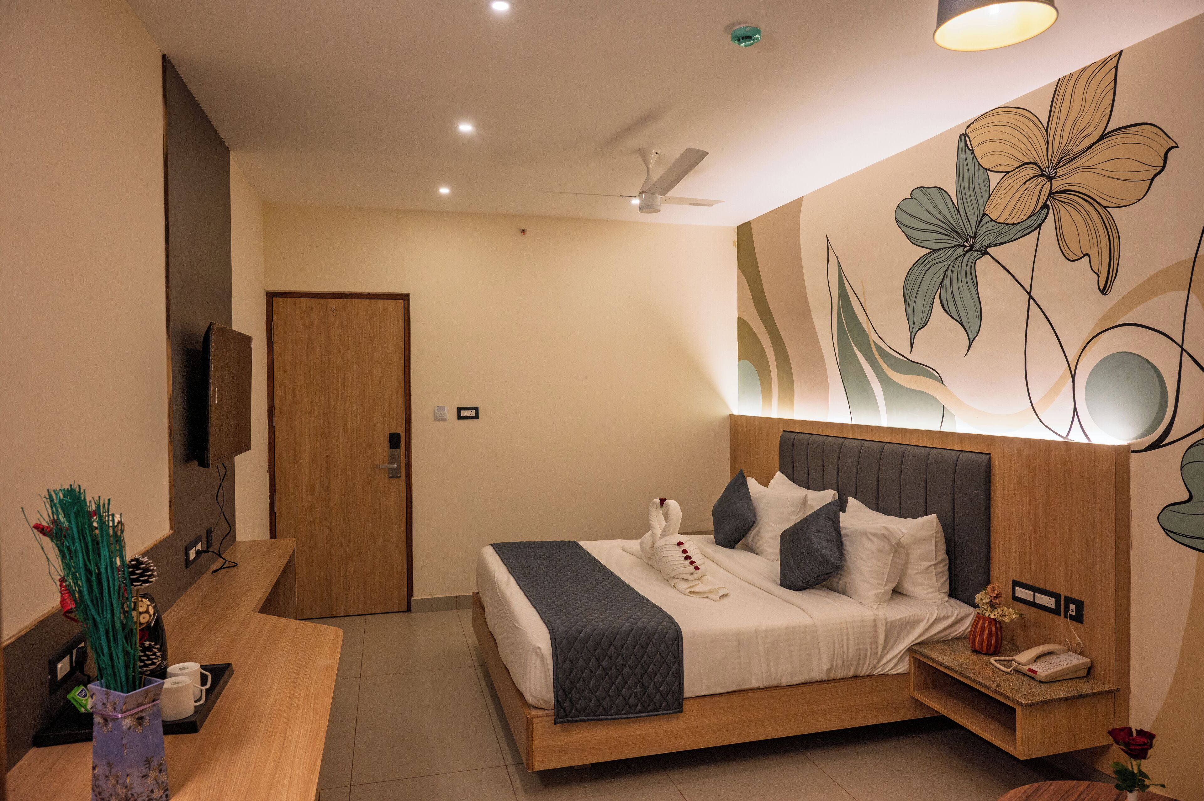 Une chambre d’hôtel équipée d’un lit, d’une table de chevet, d’œuvres d’art murales, d’un ventilateur de plafond et d’un téléviseur fixé au mur.