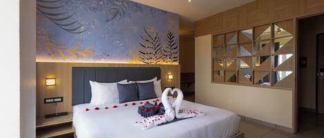 Habitación de hotel moderna con una cama grande, un ventilador de techo y un mural decorativo en la pared.