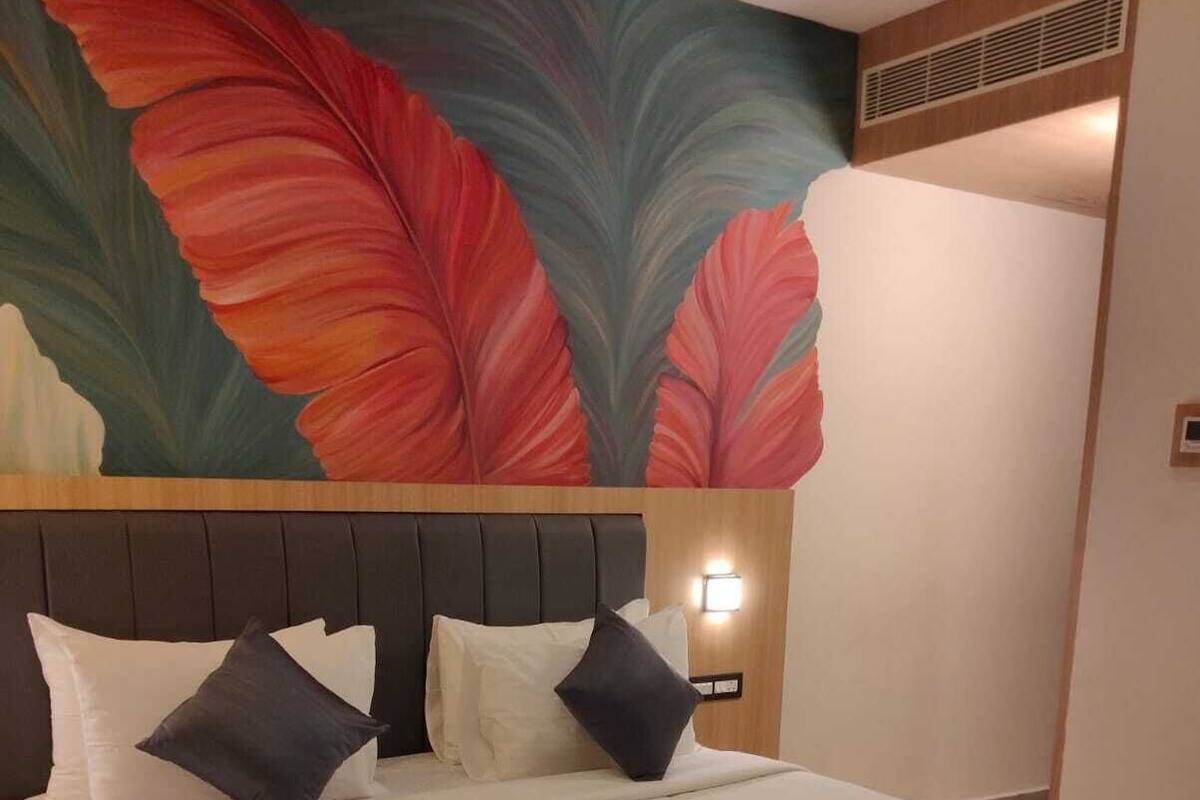 A hotel room with a large bed, a headboard with a light fixture, and a vibrant floral mural on the wall.