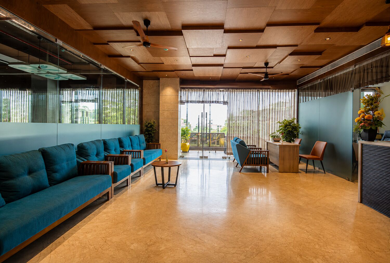 A modern lobby with a blue sofa, wooden reception desk, and a large window with curtains.