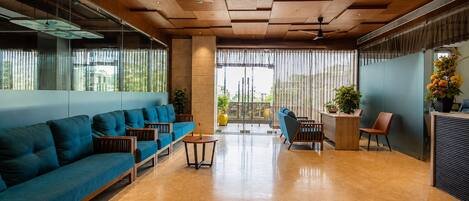 A modern lobby with a blue sofa, wooden reception desk, and a large window with curtains.