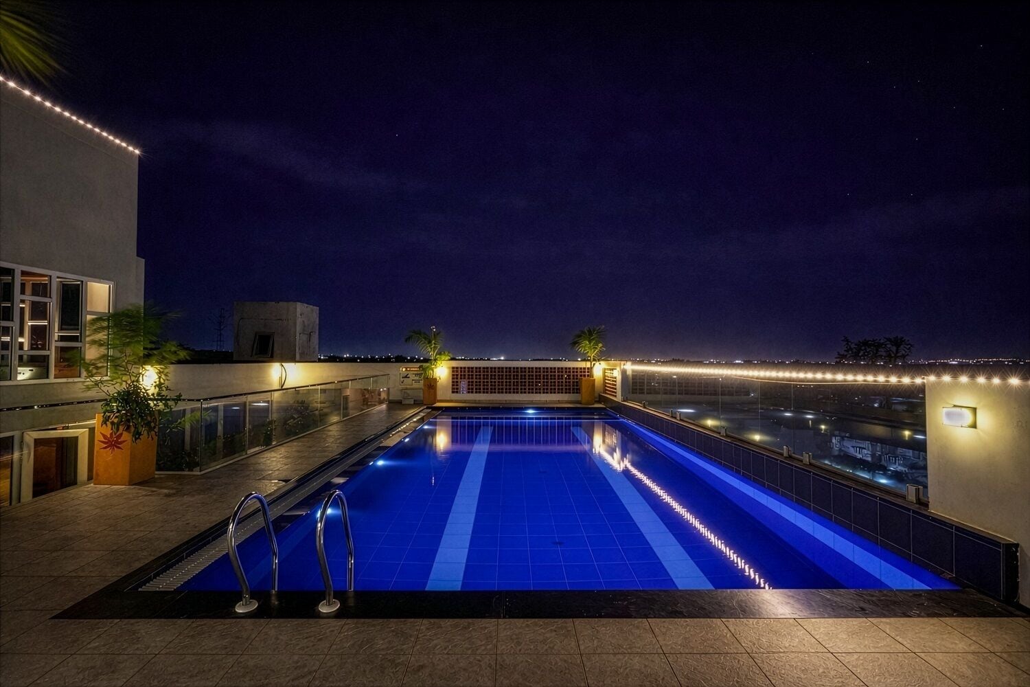 A rooftop swimming pool with a clear view of the city skyline at night.