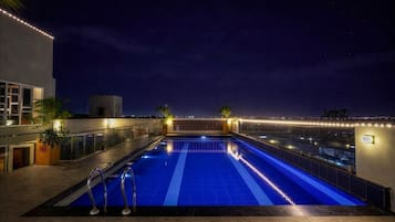 A rooftop swimming pool with a clear view of the city skyline at night.