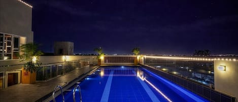Une piscine sur le toit offrant une vue dégagée sur les gratte-ciel de la ville la nuit.