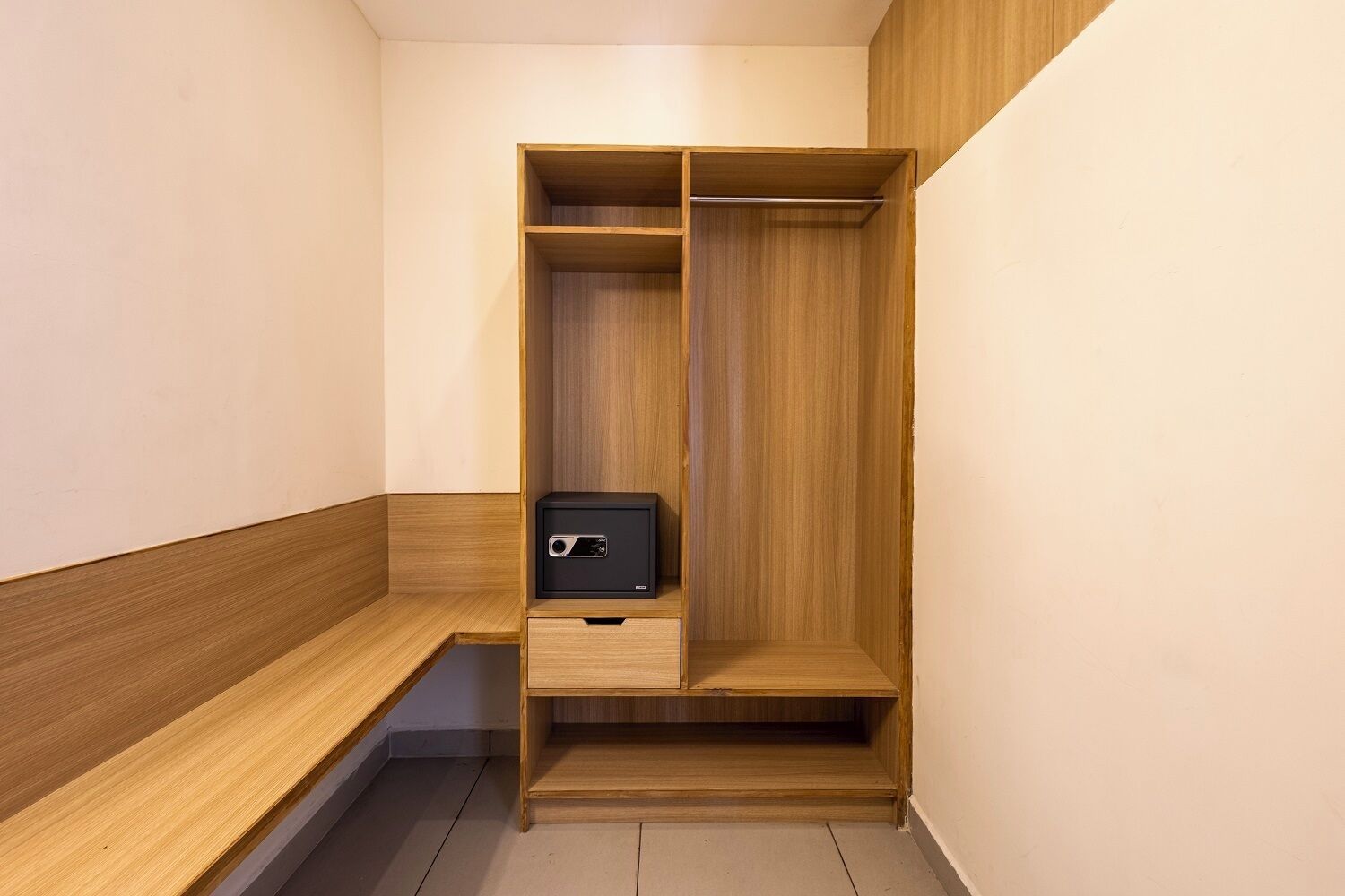 Een houten garderobe met een klein zwart kluisje, een houten bankje en één lade.