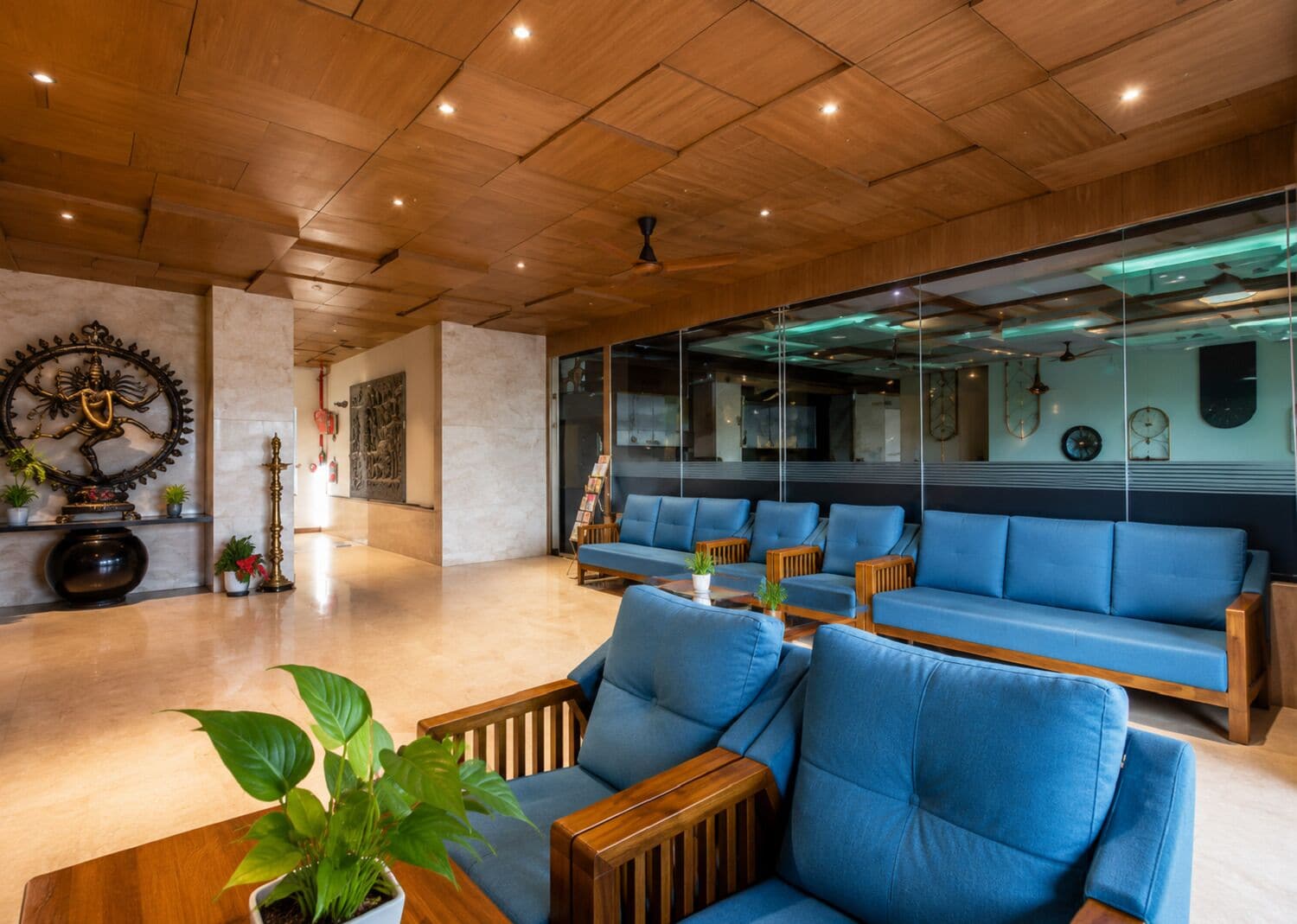 Un lobby moderno con paneles de techo de madera, áreas de descanso y elementos decorativos como obras de arte y plantas.
