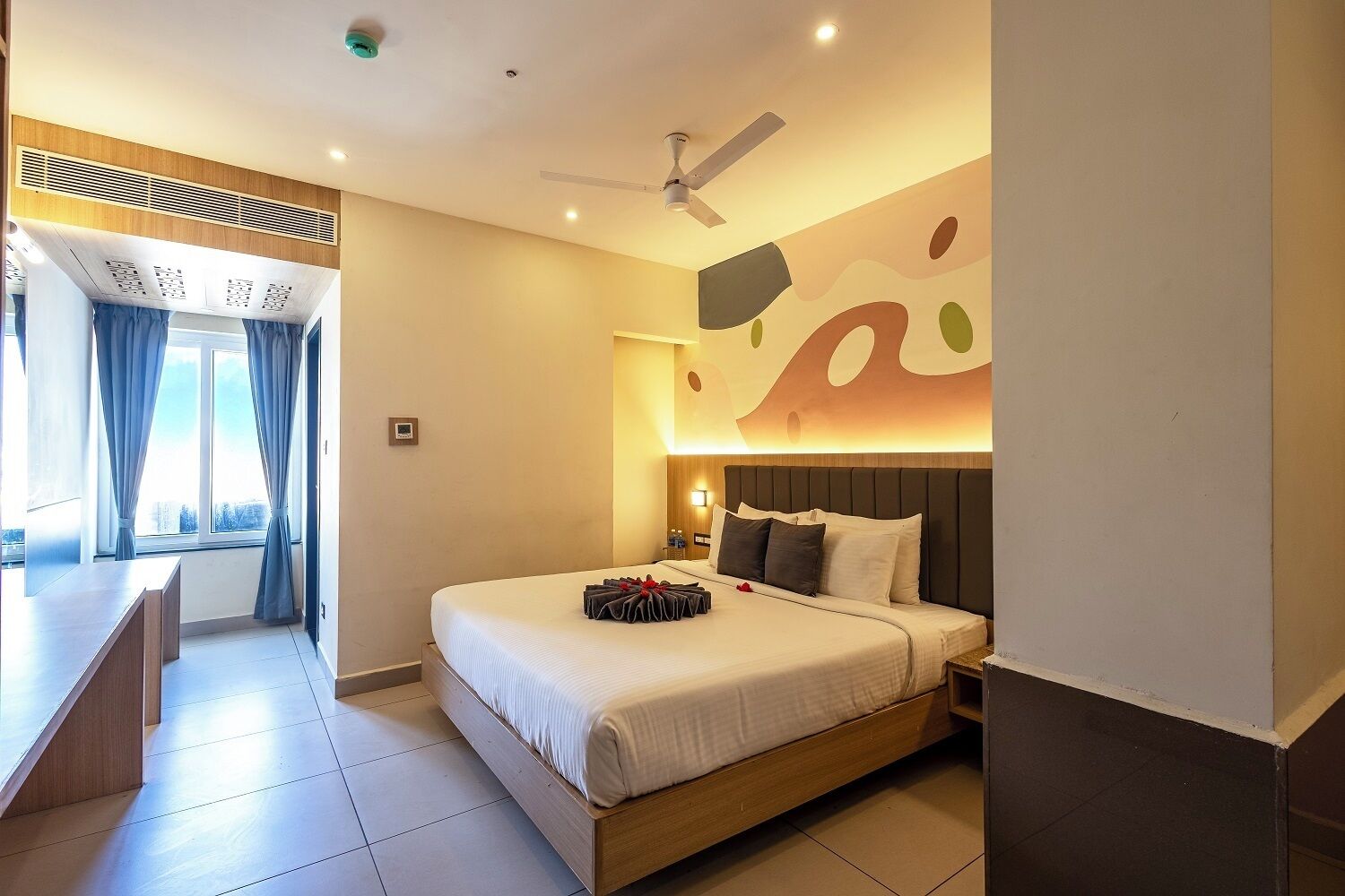 A hotel room with a bed, bedside table, and a view of the city.