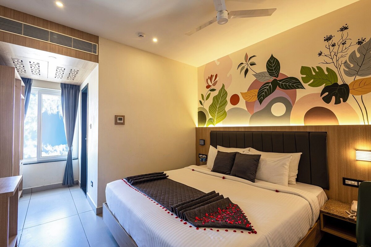 Habitación de hotel con una cama grande, un ventilador de techo, una pared con diseño de hojas y una ventana con cortinas.