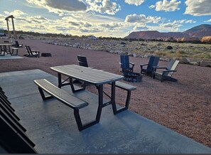 Un espace extérieur aménagé avec des tables et des chaises de pique-nique, un sol en béton et une vue sur un paysage montagneux.