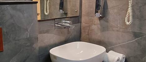 A modern bathroom with a large sink, a mirror, and two hair dryers mounted on the wall.